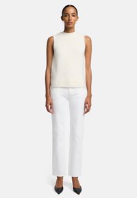 Jasnokolorowy, bezrękawnik o miękkiej fakturze, połączony z białymi spodniami prostymi oraz czarnymi szpilkami o szpiczastym nosku.