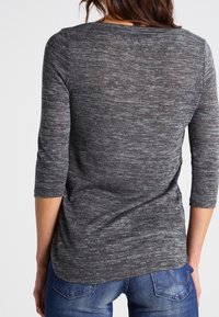 Pullover grigio testurizzato con maniche a tre quarti, presenta un orlo curvo e un motivo sottile, abbinato a jeans di denim.