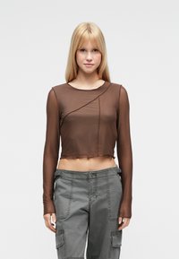 Καφέ, κοντό τοπ με μακριά μανίκια από διαφανές υλικό με στρογγυλεμένο λαιμόκοψη και ασύμμετρο σχέδιο ραφής, συνδυασμένο με γκρι παντελόνια cargo.