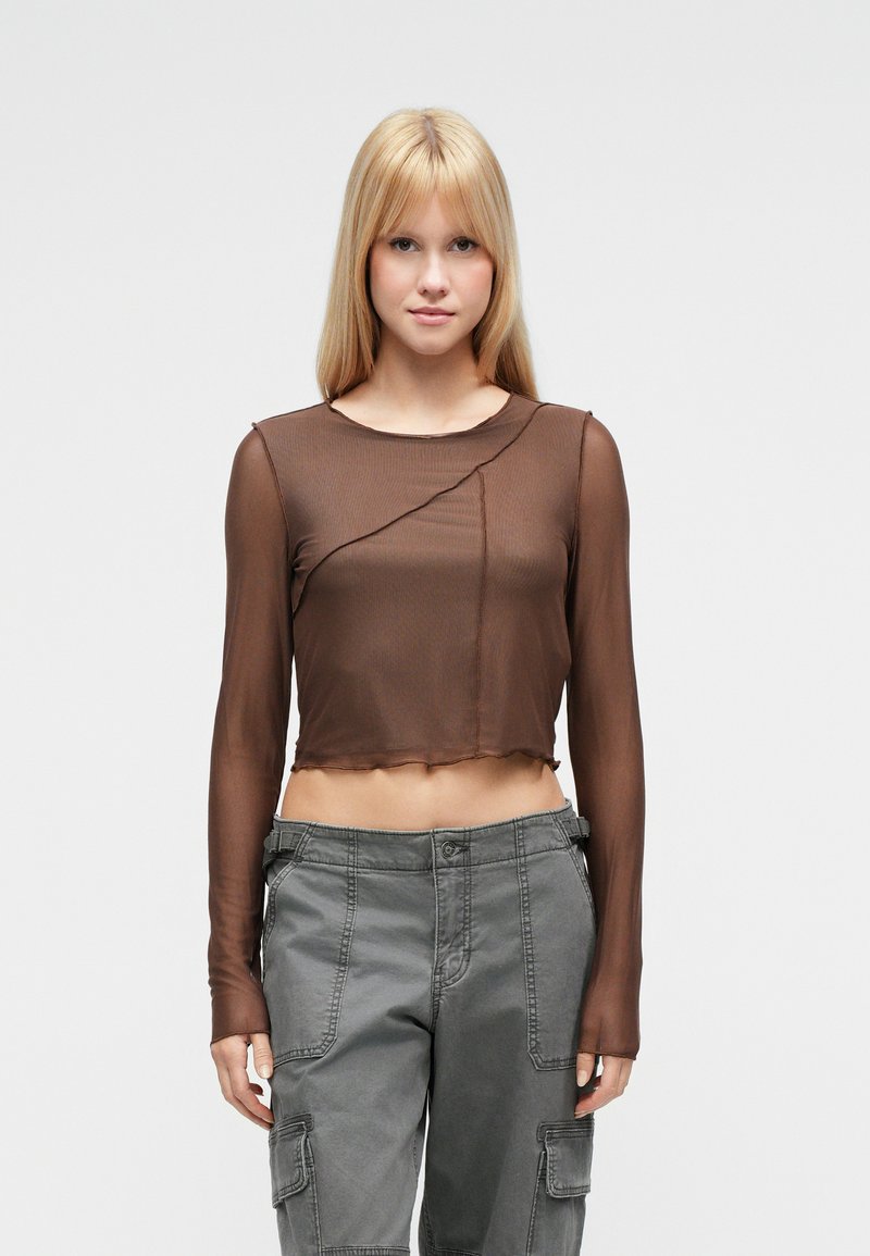 Καφέ, κοντό τοπ με μακριά μανίκια από διαφανές υλικό με στρογγυλεμένο λαιμόκοψη και ασύμμετρο σχέδιο ραφής, συνδυασμένο με γκρι παντελόνια cargo.