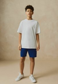 T-shirt en coton blanc, shorts texturés bleus et baskets blanches. Les shorts ont des rayures verticales ; présentent une coupe décontractée et un col rond.