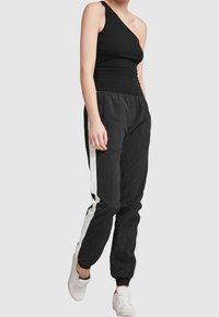 Haut noir à une épaule avec un design ajusté, associé à un jogging noir avec des rayures blanches sur les côtés. Les deux sont en tissu doux et léger.