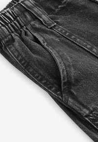 Pantaloni in denim nero con una finitura texture, dotati di una vita elastica e tasche laterali. Il materiale ha una leggera lucentezza e cuciture visibili.