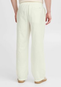 Lichtbeige linnen broek met een losse pasvorm, elastische tailleband, achterzakdetail en een gladde textuur, gecombineerd met lichte schoenen.
