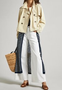 Chaqueta beige corta de doble botonadura, combinada con pantalones blancos de pierna ancha con paneles laterales a rayas en color marino. Bolsa de paja y sandalias marrones con tiras.