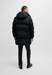 Black padded parka with a hood, featuring a quilted design, elastic cuffs, and a relaxed fit, shown from the back.