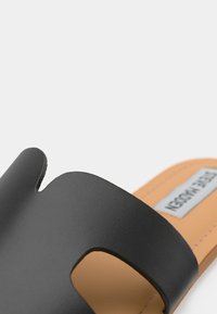 Sandales à glissière en cuir noir avec un design découpé, texture lisse et semelle intérieure beige clair. Étiquette de marque argentée sur la semelle intérieure.