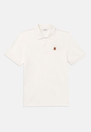 Kortermet, hvit polo skjorte i myk bomullsstoff. Har en placket med tre knapper og en liten brodert logo i brunt på brystet.