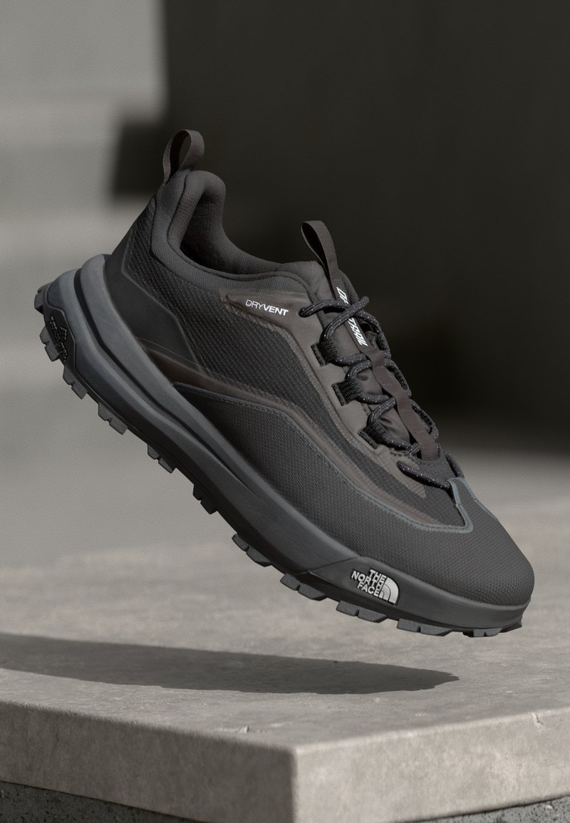 Zapatilla de trail running negra con parte superior texturizada, sistema de cordones y suela de goma gruesa. Presenta la marca "DRYVENT" en el lateral.