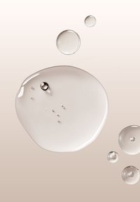 Ein klarer, gelartiger Flüssigkeit mit einer glatten Textur und einem hellbeigen Farbton, die verschiedene Größen von Wassertropfen auf einem sanften Farbverlaufshintergrund zeigt.
