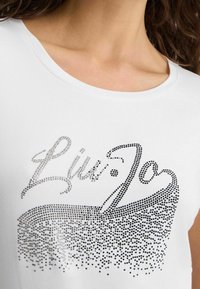 Camiseta blanca de manga corta con escote redondo que presenta un diseño degradado en negro y plateado brillante con la palabra "Liu Jo" escrita en rhinestones.