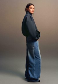 Donkerblauwe oversized sweatshirt met hoge kraag, gecombineerd met lichtblauwe wide-leg jeans met een gradient effect en achterzakken.