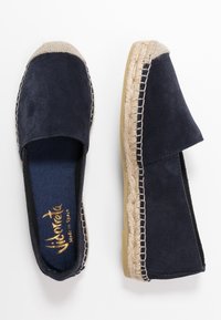 Námořnické surové espadrilky s juta podešví, otevřenými boky a elastickými detaily. Interiér má texturovanou látku se zlatým logem.