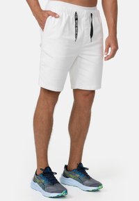 Hvide shorts med elastisk talje og sort snor, med to sidelommer og en glat tekstur. Sættes sammen med grå træningssko.