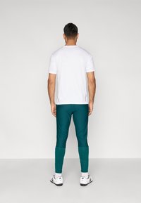 Λευκό κοντομάνικο μπλουζάκι, πετρόλ στενά παντελόνια με υφασμάτινη υφή στα κάτω μέρη, φορεμένα με λευκά αθλητικά παπούτσια. Απλός και λειτουργικός σχεδιασμός.