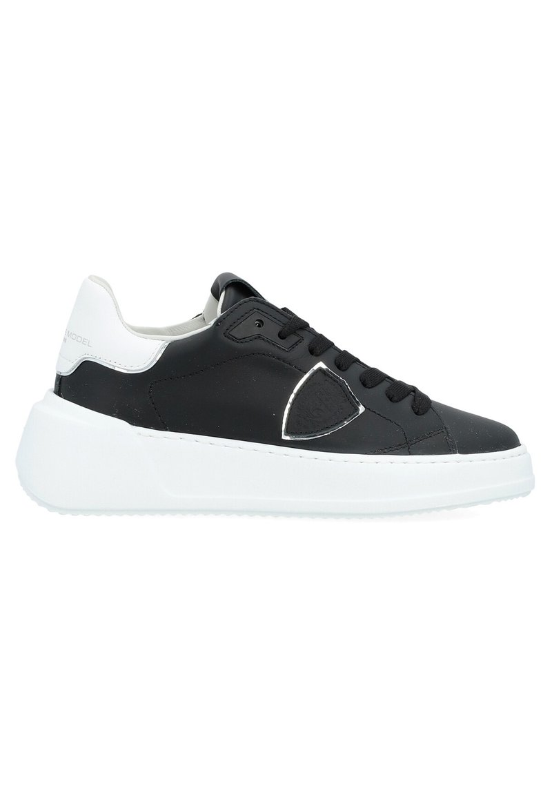 Black and white sneaker with a smooth leather upper, featuring a rounded toe, thick white sole, and subtle logo detail on side.