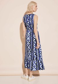 Robe sans manches bleue à motifs géométriques, avec un ourlet froncé et une taille cintrée. Associée à des baskets blanches.