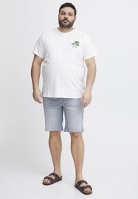 Bílý bavlněný tričko s grafikou palmy; světle modré denimové šortky; hnědé sandály; volný střih; neformální letní outfit.