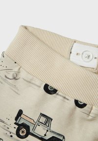 Ceinture en tissu beige avec texture côtelée et fermeture à bouton, ornée d'un imprimé d'un camion vintage et de roues sur un fond clair.