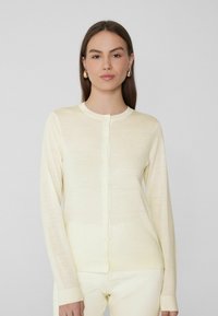 Cárdigan tejido de color amarillo claro con mangas largas, cuello redondo y cierre frontal con botones. Textura suave con puños y dobladillo acanalados.