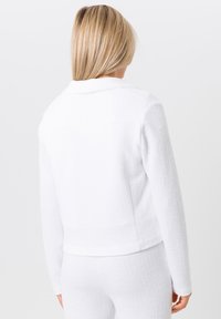 Weißes strukturiertes Jacket mit Kragen und langen Ärmeln, mit einer taillierten Passform. Getragen mit passenden weißen Unterteilen.