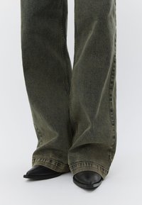 Olivengrønne bukser med vide ben og en let struktureret finish, kombineret med sorte ankelstøvler med spidst tåparti i mat læder.