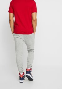 Camiseta roja de manga corta, pantalones de chándal grises y zapatillas deportivas multicolores con detalles rojos. Conjunto casual de corte holgado, costuras visibles.