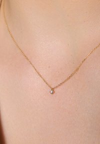 Złoty naszyjnik z małym, okrągłym wisiorkiem wysadzanym diamentem. Łańcuszek ma delikatny, ogniwkowy wzór z polerowanym wykończeniem.