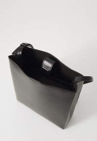 Black leather tote bag with a structured design, open top, and flat straps. Smooth texture with minimal hardware and a simple silhouette.