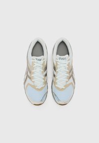 Ελαφριά αθλητικά παπούτσια με επάνω μέρος από δίχτυ σε λευκό και ανοιχτό μπλε με μπεζ λεπτομέρειες, επίπεδα κορδόνια και μαλακή γκρίζα σόλα.