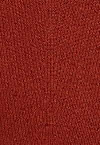 Tessuto a maglia a coste in una ricca tonalità di rosso. La texture appare morbida con dettagli di filato fine, creando un motivo uniforme in tutta la superficie.