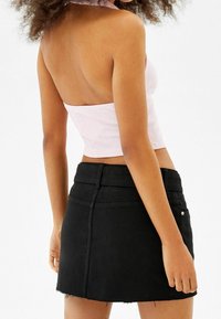 Ljust rosa ribbat crop-top med en figurnära design och rak halsringning, i kombination med en svart denim minikjol med fransad fåll.