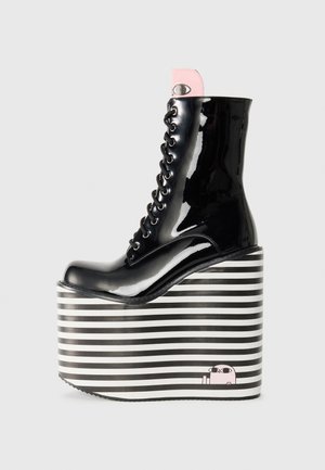 Botine negre din piele lactică, cu talpă platformă cu dungi alb-negre, având accente roz și un detaliu grafic în stilul desenelor animate.