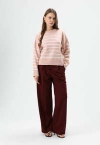 Lichtroze gestreepte trui met een ronde hals, oversized pasvorm, geribbelde zoom en manchetten. Gecombineerd met bordeauxrode broek met wijd uitlopende pijpen.