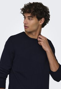 Marineblauwe lange mouw trui in een soepele textuur. Heeft een ronde halslijn en aansluitende manchetten, met een slanke silhoeet en een minimalistisch ontwerp.
