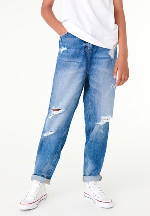 Lysblå slidte jeans med huller, løs pasform og oprullede manchetter, parret med hvide sneakers. Glat denimtekstur, afslappet design.