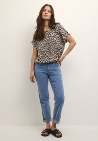 Leopardmönstrad blus i lätt tyg, kombinerad med uppvikta ljusblå jeans och svarta sandaler med guldspännen.