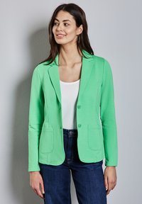 Groene katoenen blazer met een op maat gemaakte uitstraling, sluiting met één knoop, scherpe revers en twee voorzakken. Draagt over een witte top.