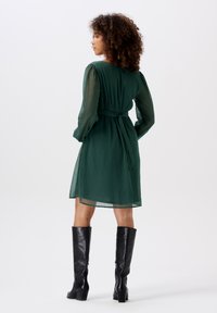Green, semi-sheer dress with long, puffed sleeves and a cinched waist, paired with knee-high black leather boots.