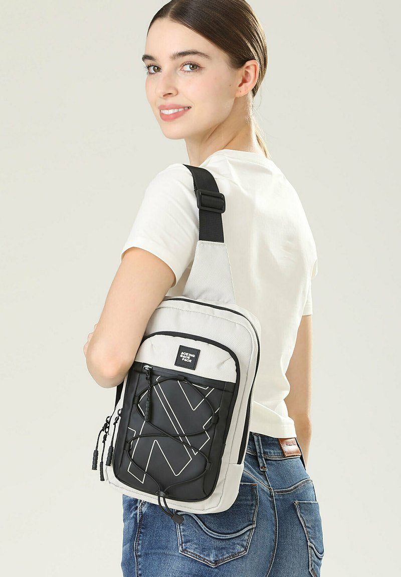 Borsa a tracolla in grigio chiaro e nero, caratterizzata da un motivo geometrico, con tracolla regolabile e scomparti con zip per la conservazione.