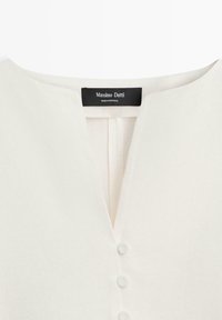 Kark wykonany z ecru z wycięciem w kształcie litery V, poniżej trzy guziki obciągnięte tkaniną oraz czarna metka Massimo Dutti przyszyta wewnątrz kołnierza.