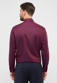 Camicia bordeaux a maniche lunghe con una texture liscia, taglio su misura e polsini con bottoni, vista da dietro, che mette in risalto il colletto e la cucitura della spalla.
