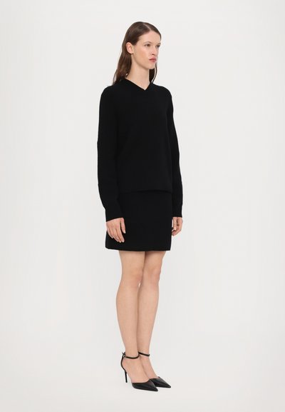 Maglione nero a maglia con scollo a V, abbinato a una mini gonna nera e tacchi a punta neri. Design semplice e coerente.