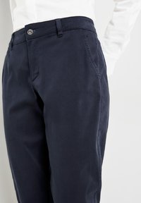 Navy blue cotton blend trousers featuring a straight cut, belt loops, a front clasp with a branded button, and side pockets.