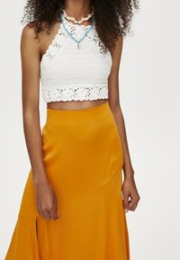Top corto de ganchillo blanco con detalle de encaje y falda maxi amarilla de satén con dobladillo asimétrico y abertura lateral.