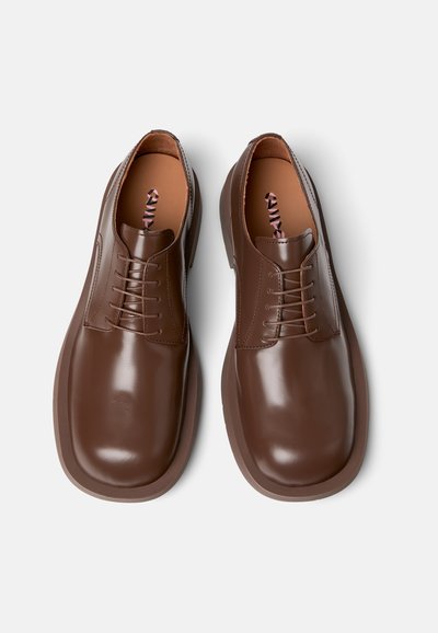 Scarpe in pelle marrone con lacci, dal finish liscio, punta rotonda e dettagli di cuciture sottili, con solette marroni e un accento decorativo a motivi.