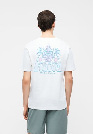 Άνδρας στέκεται με την πλάτη γυρισμένη, φοράει λευκό μπλουζάκι με παστέλ φοίνικες, γραφικό ματιού και το κείμενο «Volcom Original Stone Co» στην πλάτη.