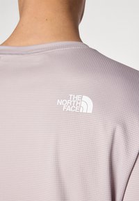 Heled lilla lühikese varrukaga särk, millel on ruuduline tekstuur ja valge "The North Face" logo, mis asub seljal kaela lähedal.