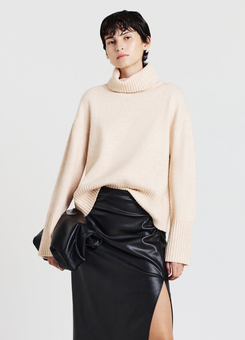 Beige gestrickter Rollkragenpullover mit gerippten Bündchen, kombiniert mit einem figurbetonten schwarzen Lederrock mit seitlichem Schlitz. Glatte, weiche Textur.