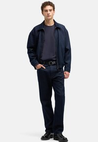 Ciemna kurtka dżinsowa z kołnierzem, zestawiona z granatowym t-shirtem i dopasowanymi spodniami. Całość dopełnia czarny pasek i buty.